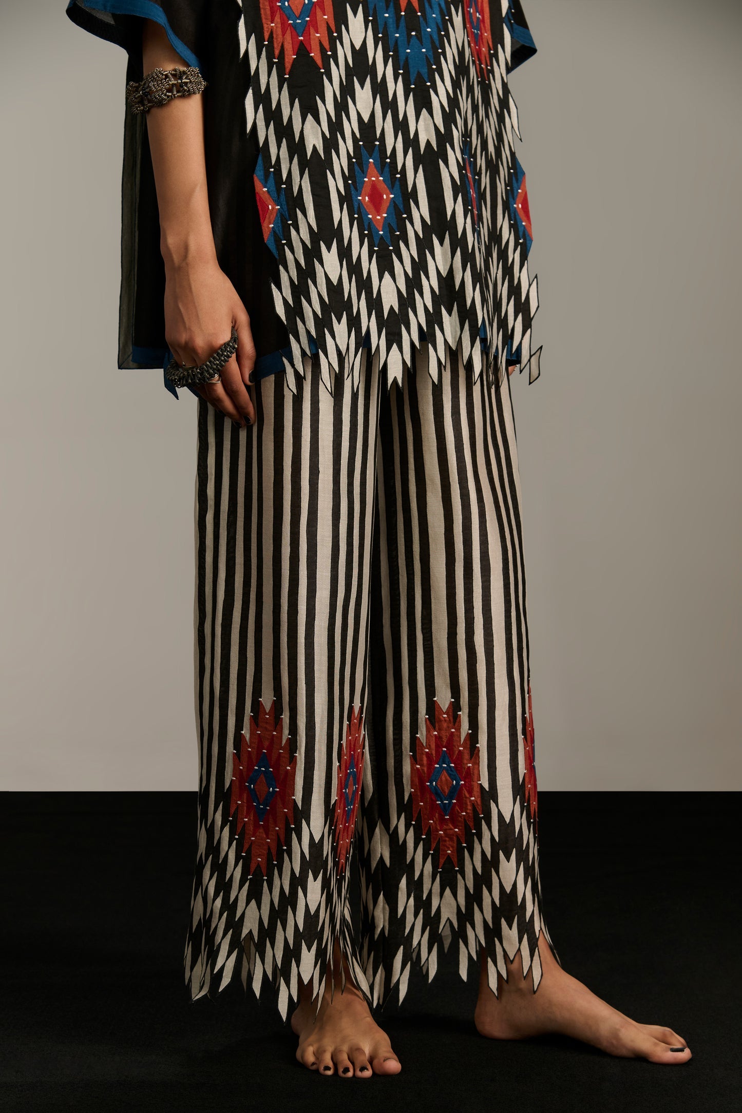 Person wearing a patterned outfit with black, white, and red design on a plain background