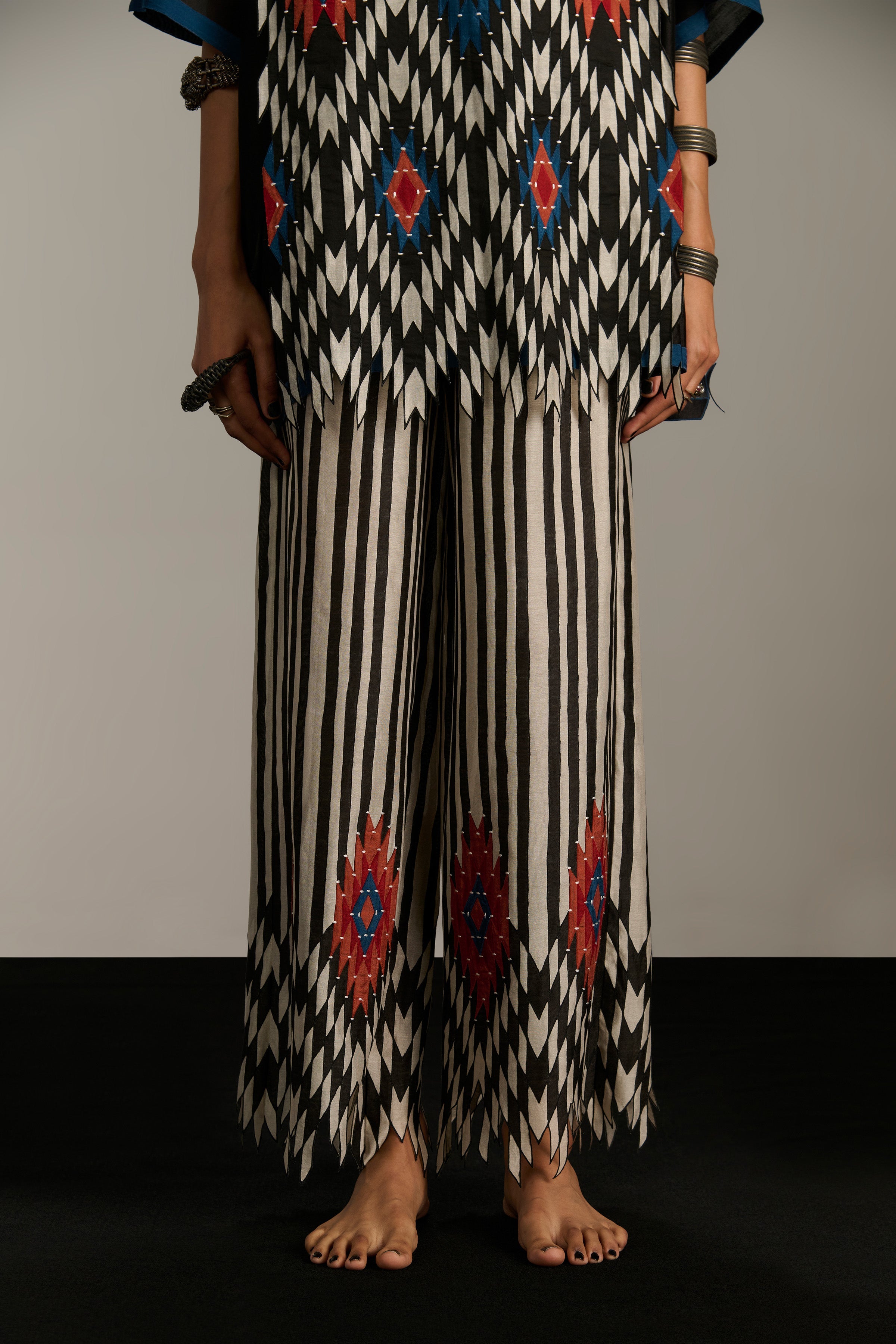 Person wearing a black and white patterned outfit with red and blue accents on a plain background