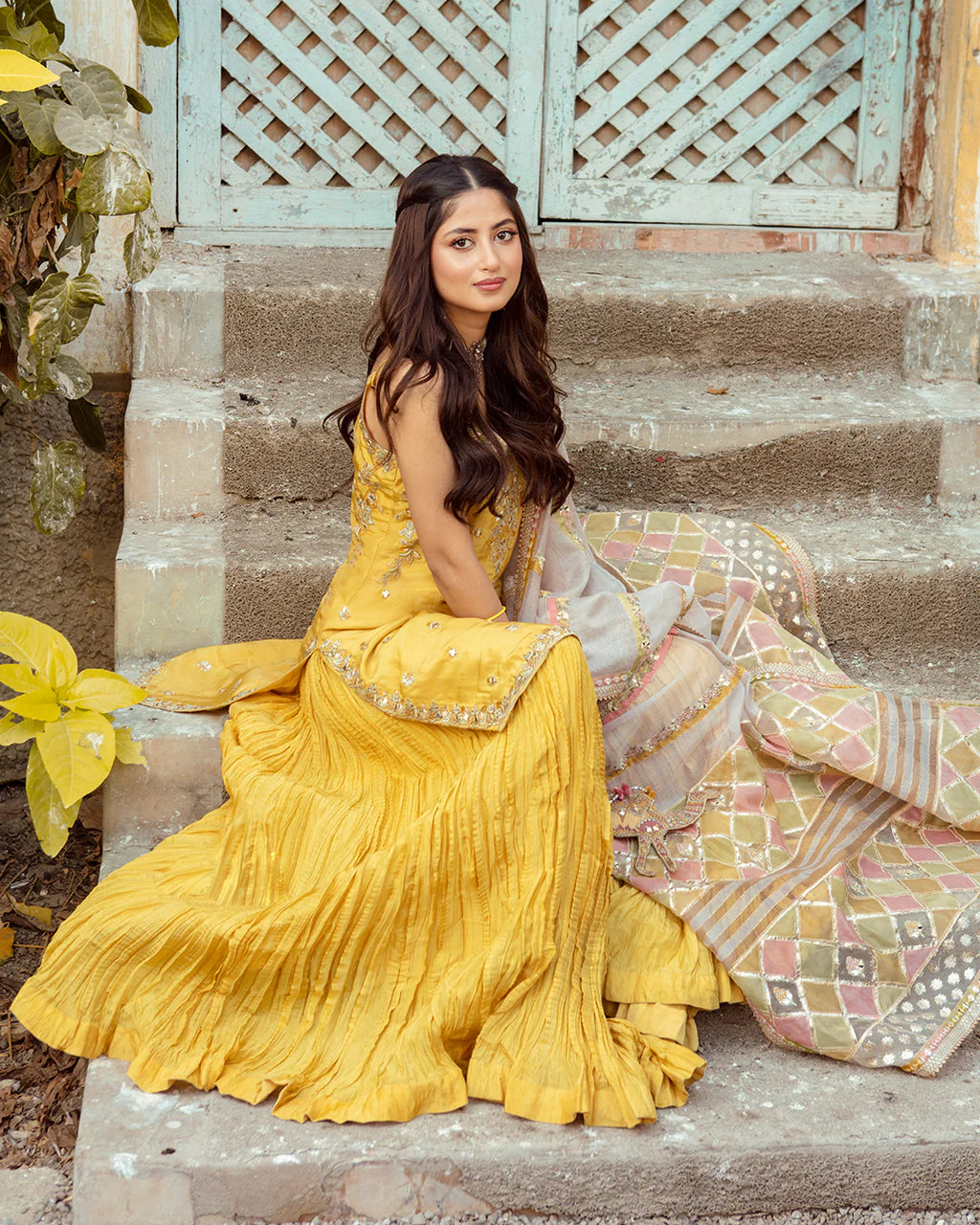 Woman in a yellow traditional outfit sitting on stone steps with decorative elements.