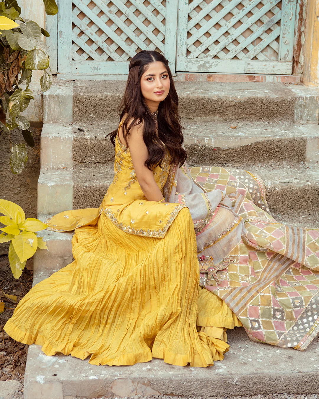 Woman in a yellow traditional outfit sitting on stone steps with decorative elements.