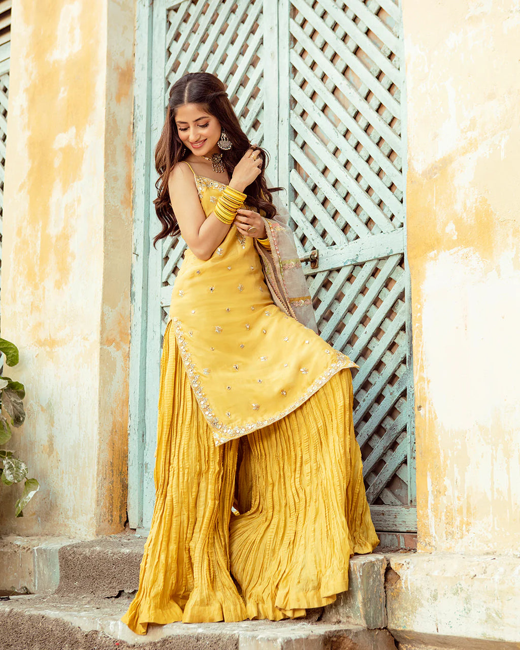 Woman in a yellow saree standing in front of a decorative door.