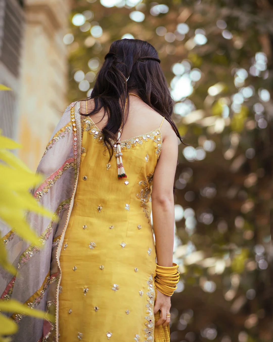 Woman in a yellow traditional outfit with floral decorations, standing outdoors.