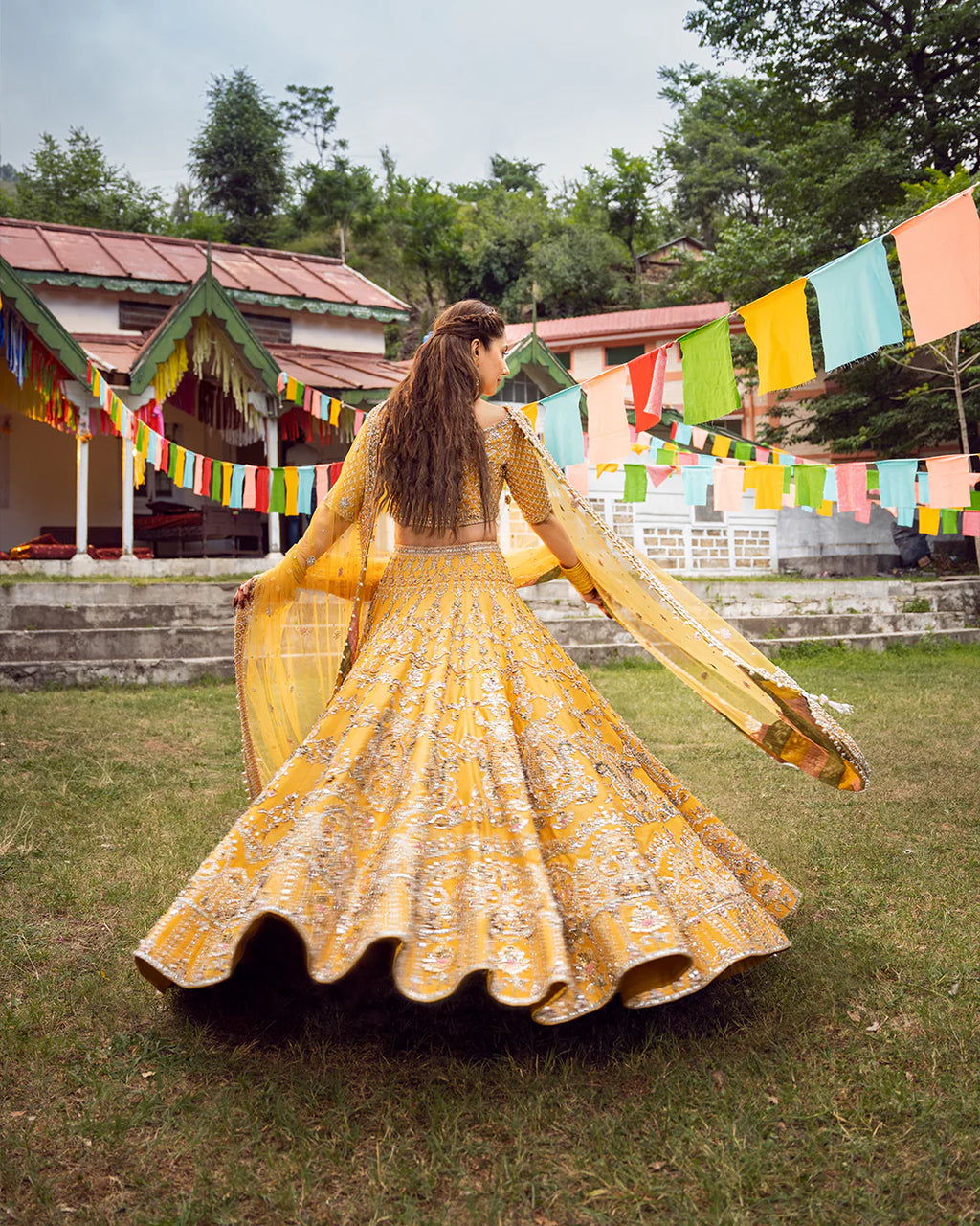 Woman in a yellow traditional outfit standing outdoors with colorful flags in the background