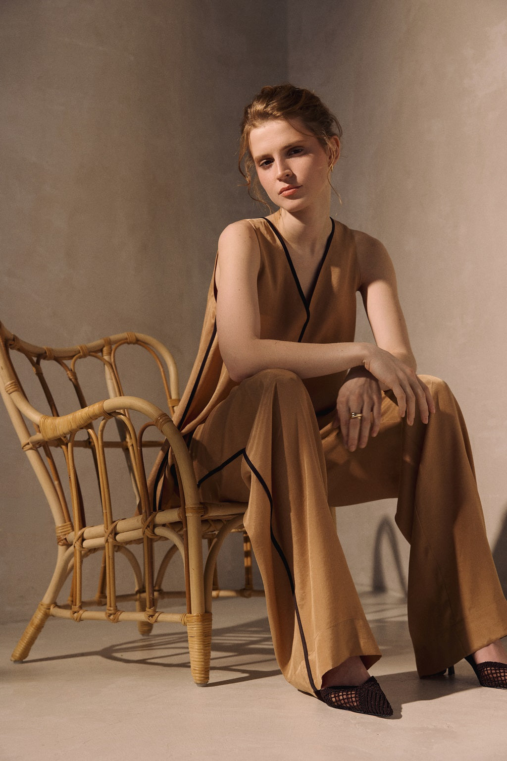 Woman in a brown outfit sitting on a wicker chair against a plain background