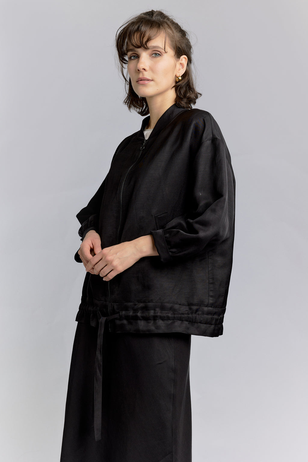 Woman wearing DEITY Midnight Bomber Wrap with white wide-leg trousers and black sunglasses.