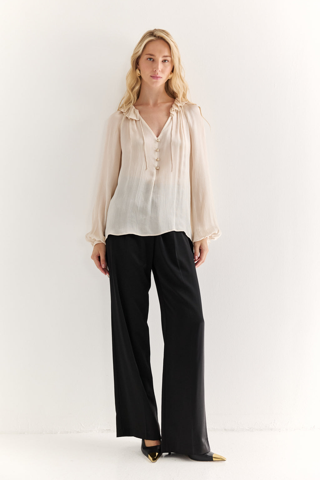Woman wearing a beige blouse and black pants on a white background