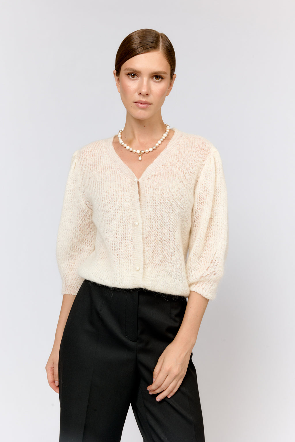 Woman wearing a cream sweater and black pants on a light gray background