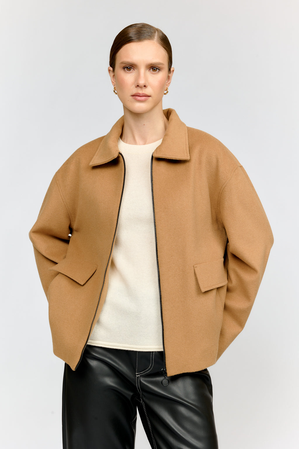 Person wearing a tan coat over a white shirt and black pants on a light gray background