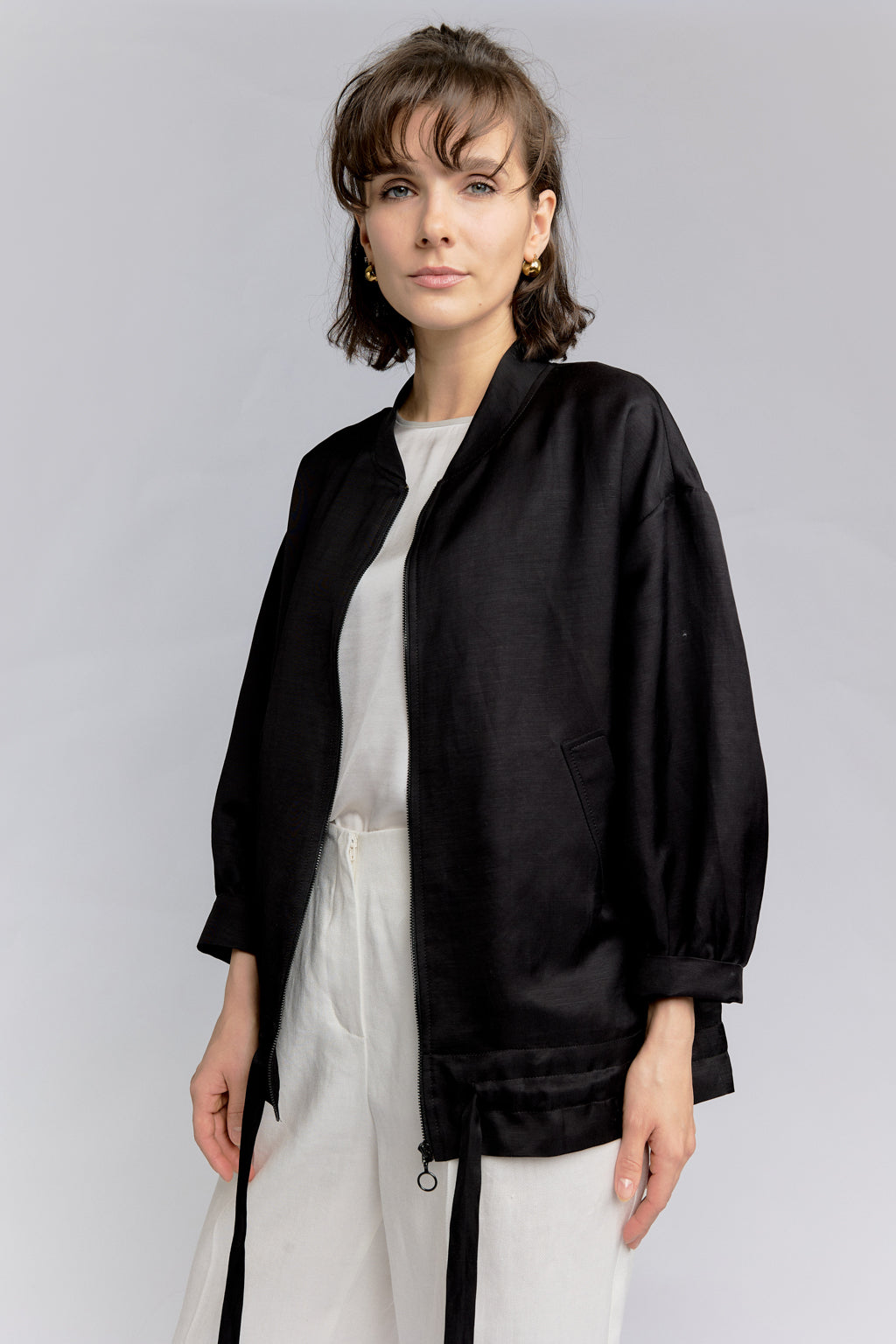 Woman wearing DEITY Midnight Bomber Wrap with white wide-leg trousers and black sunglasses.