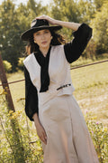 Woman in a stylish outfit with a hat standing in a field.