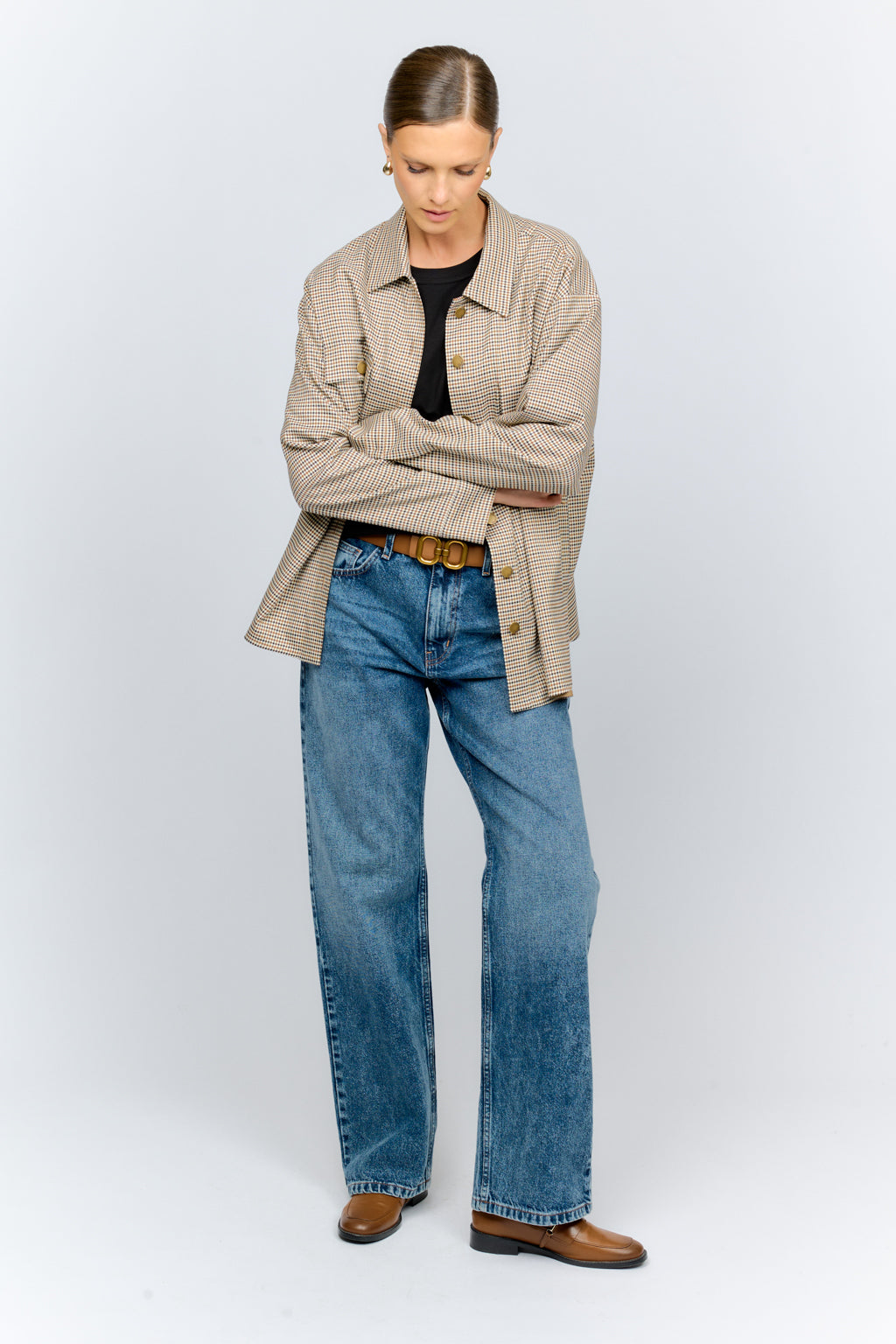 Person wearing a beige jacket, black shirt, blue jeans, and brown shoes on a white background