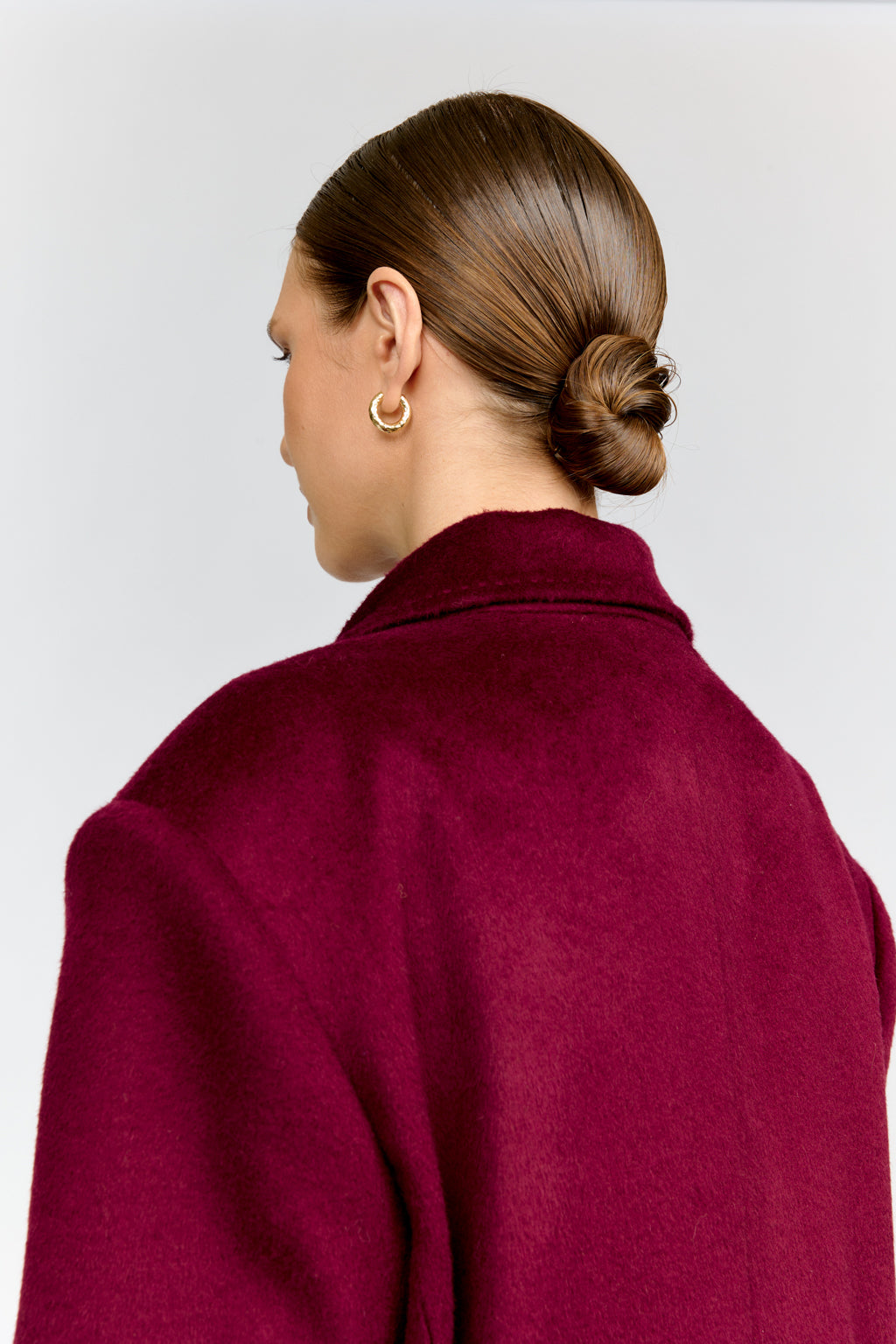 Person wearing a burgundy coat with a plain background