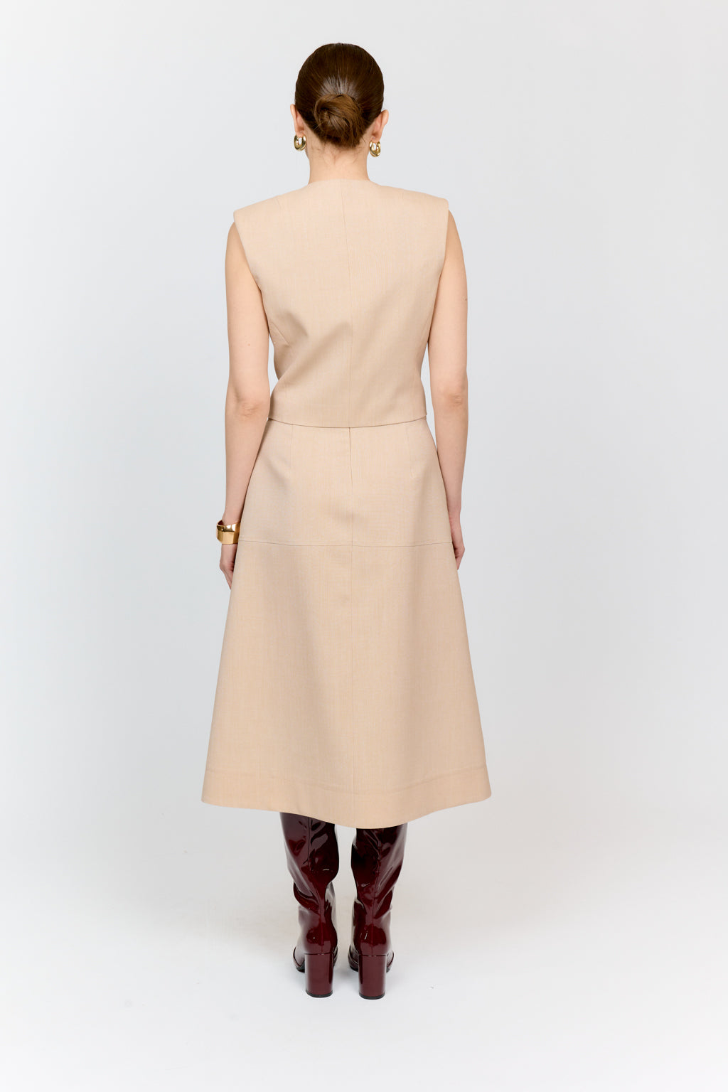 Woman wearing a beige dress with burgundy knee-high boots on a white background