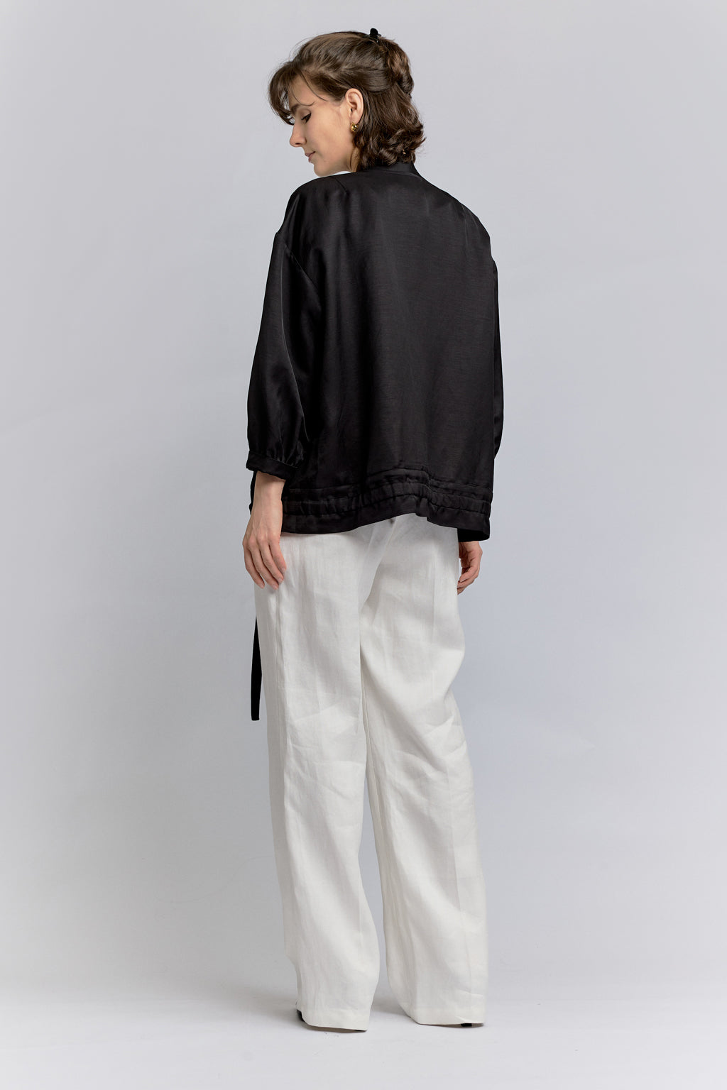 Person wearing a black jacket and white pants on a light gray background