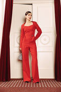Woman in a red outfit standing in a room with red curtains and white walls.