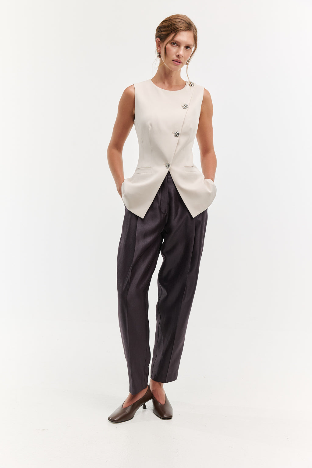 Woman wearing a white sleeveless top and dark pants on a white background