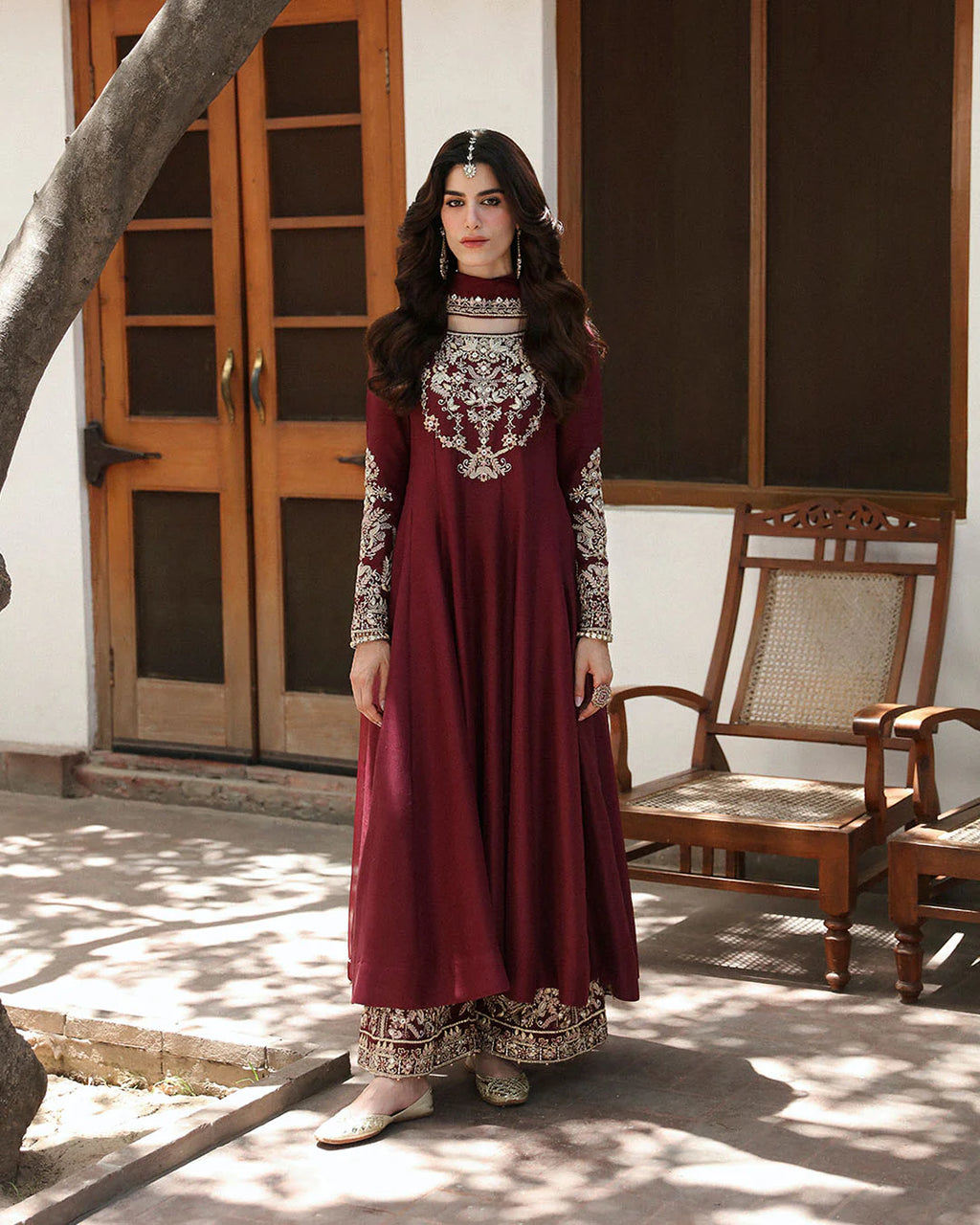 Woman in a maroon traditional outfit with white embroidery standing outdoors.