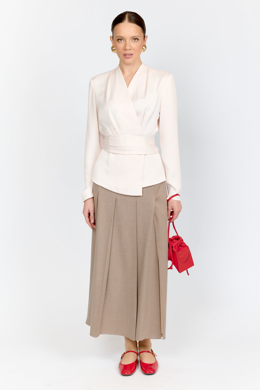 Woman wearing a white blouse and beige skirt with red shoes and handbag on a white background