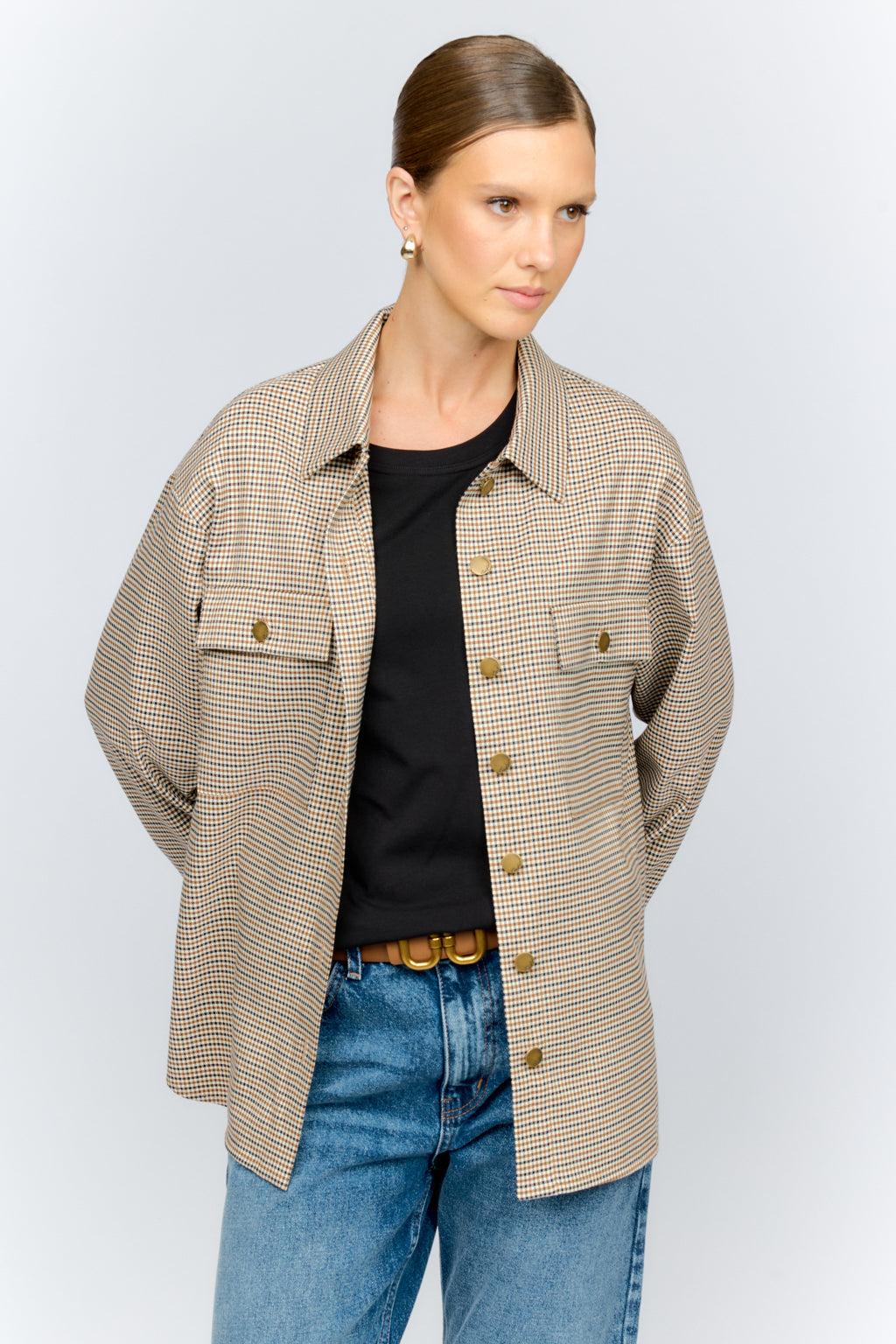 Woman wearing a beige checkered shirt over a black top and blue jeans on a white background