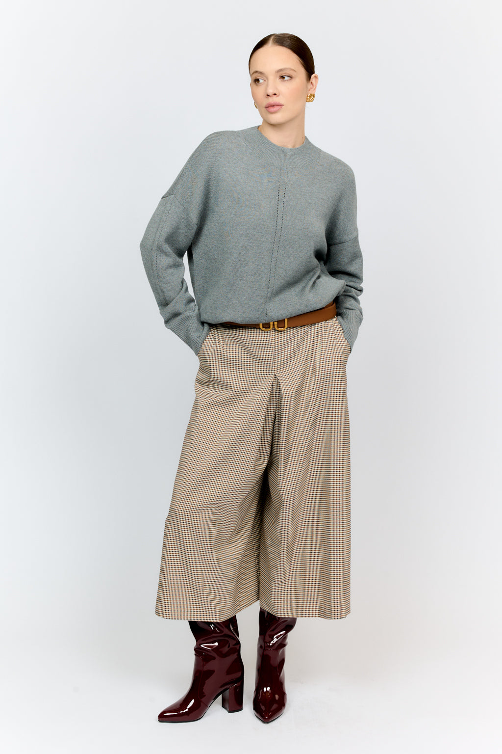 Woman wearing a gray sweater, beige wide-leg pants, and brown boots on a white background