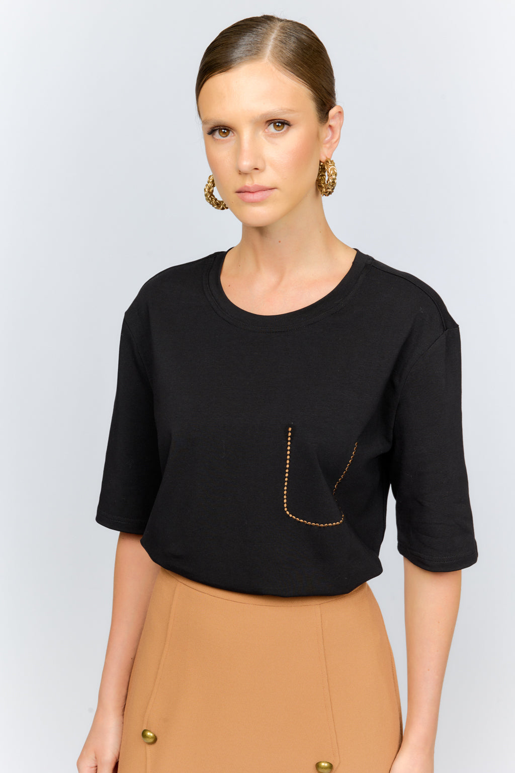 Woman wearing a black top with a gold pocket detail on a light gray background