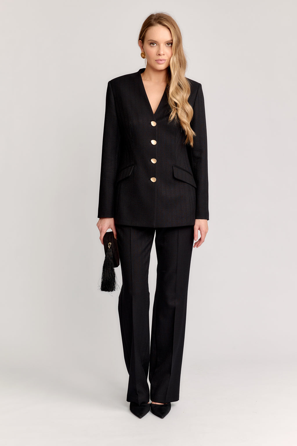 Woman wearing a black suit with a white background Front view of the DEITY Obsidian sackcloth jacket showing the lapel-less V-neck.