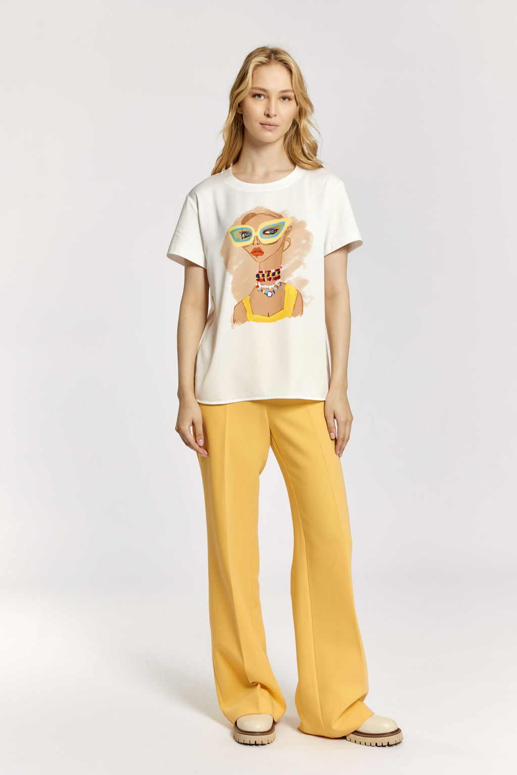 Woman wearing a white t-shirt with a graphic design and yellow pants on a white background