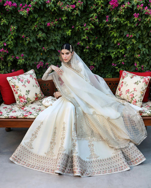 Woman in a traditional outfit sitting on a floral-patterned couch with greenery in the background