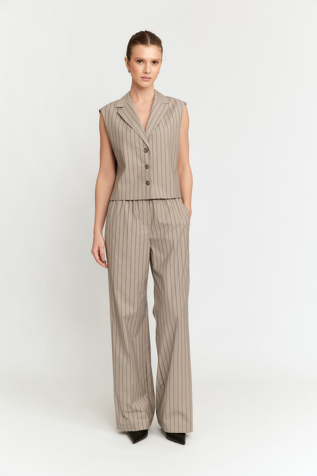 Woman wearing a beige pinstripe vest and pants on a white background