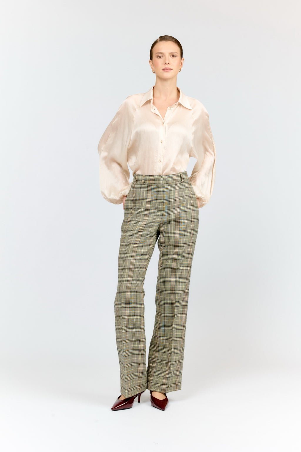 Woman wearing a light-colored blouse and plaid pants on a white background