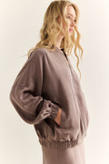 Woman wearing a brown bomber jacket on a plain background