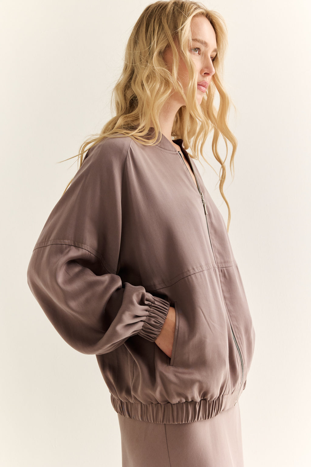 Woman wearing a brown bomber jacket on a plain background