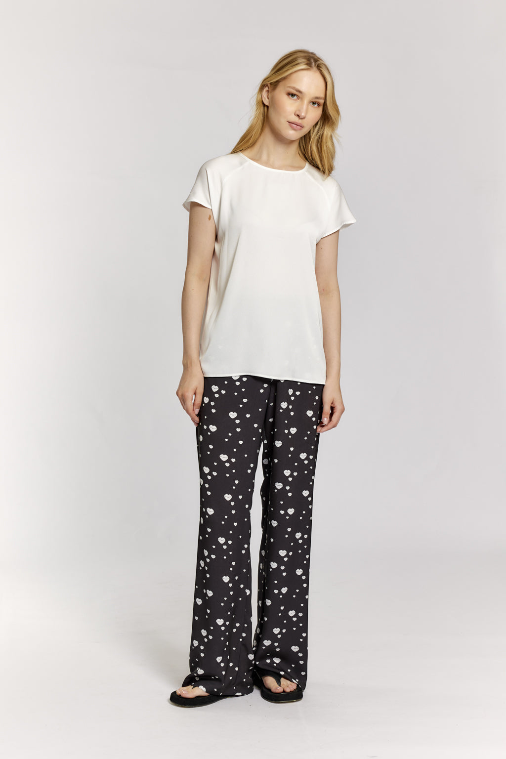 Woman wearing a white top and black patterned pants on a light gray background