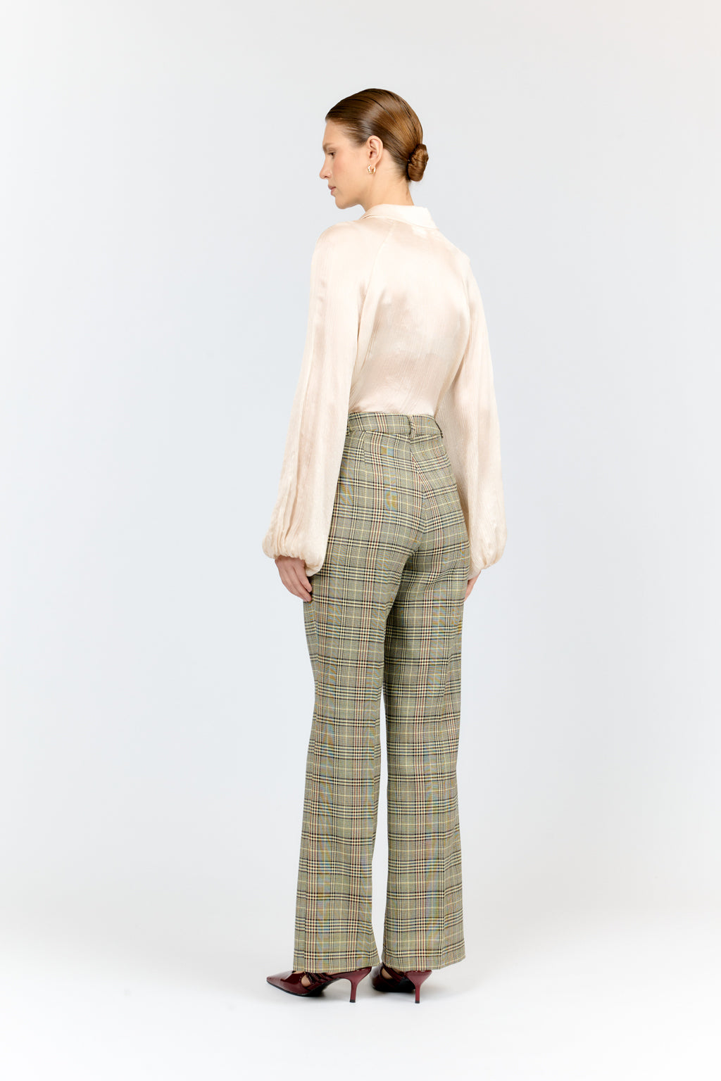 Woman wearing a light pink blouse and plaid pants on a white background