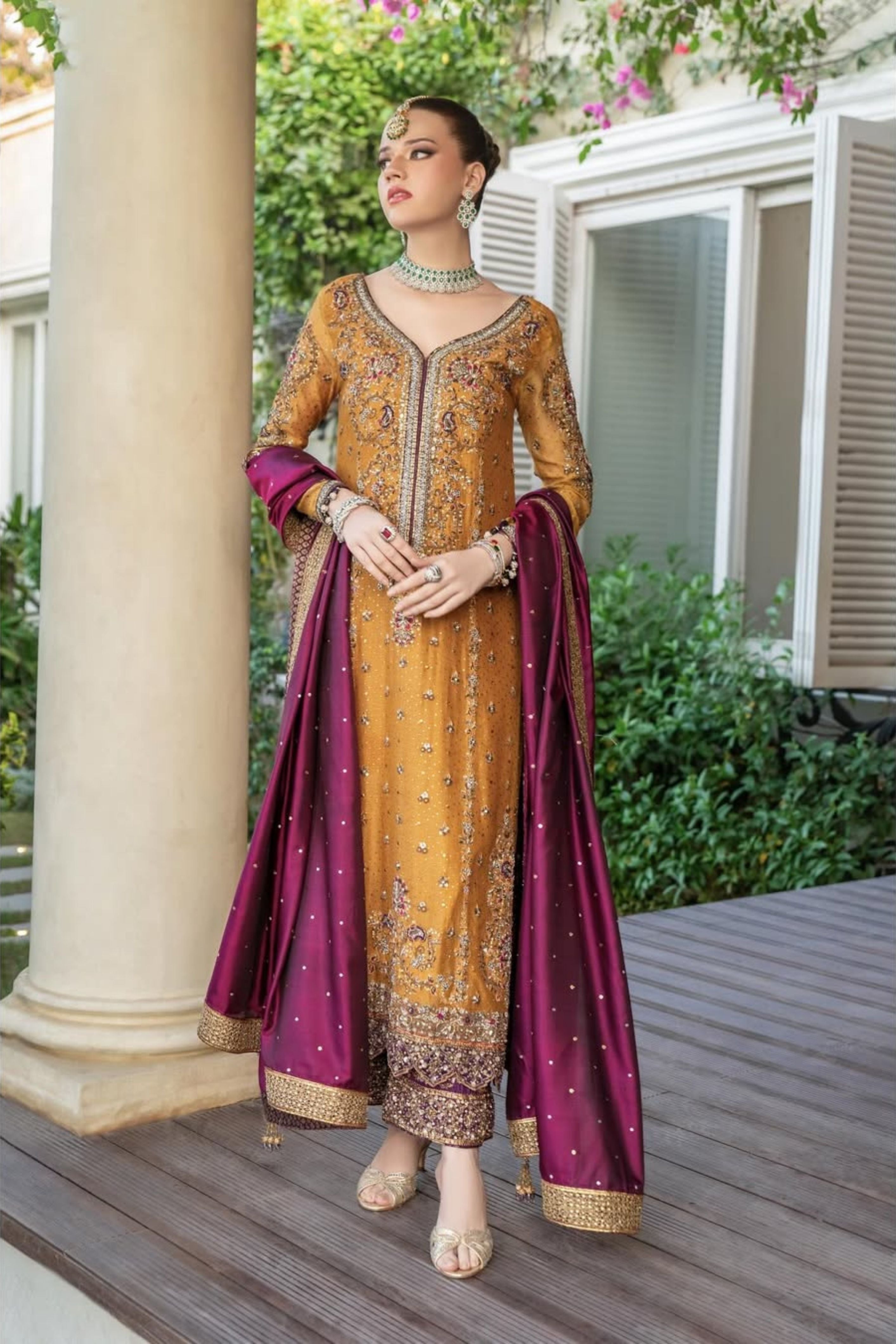Woman in traditional embroidered outfit with a purple dupatta standing outdoors.