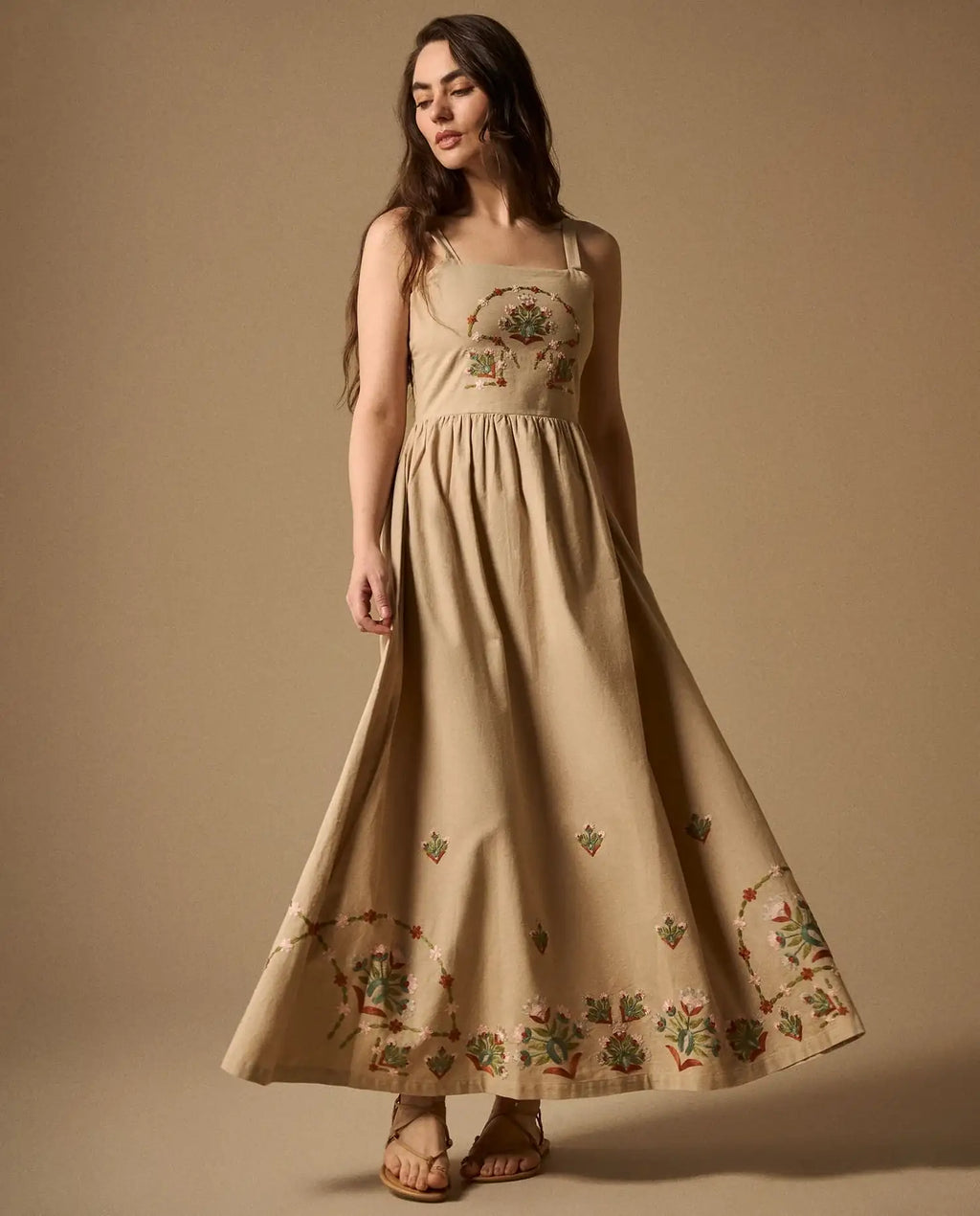 Woman wearing AYRA long beige dress featuring multicolored handcrafted floral embroidery on the structured bodice and hemline