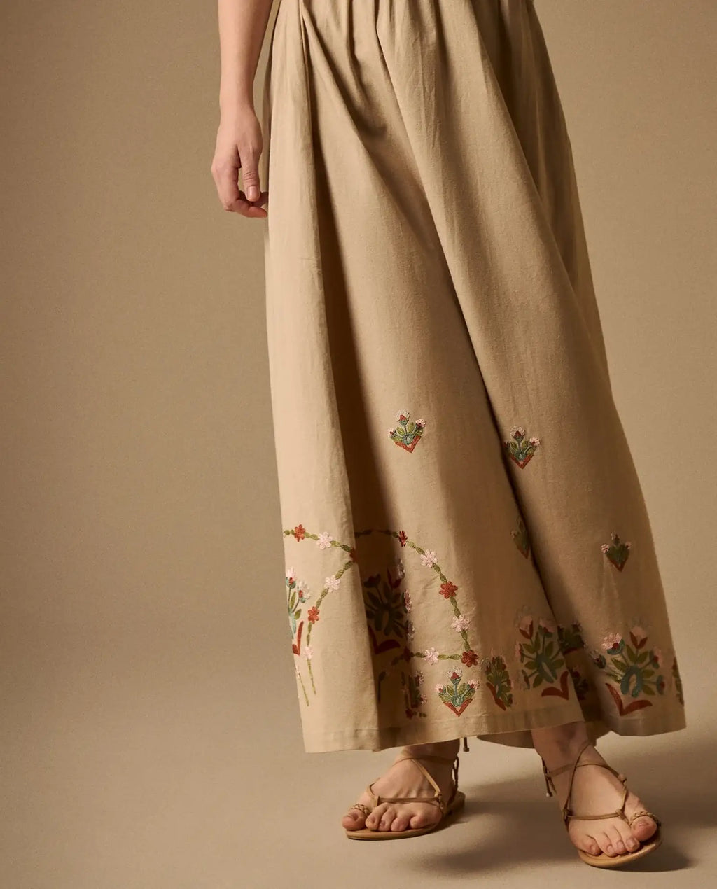 Woman wearing AYRA long beige dress featuring multicolored handcrafted floral embroidery on the structured bodice and hemline