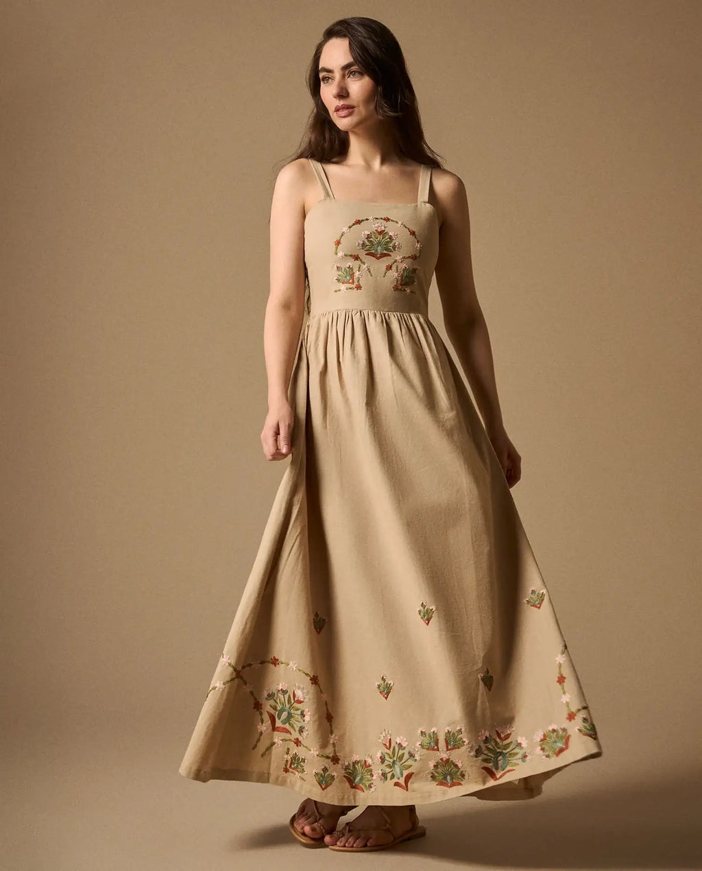 Woman wearing AYRA long beige dress featuring multicolored handcrafted floral embroidery on the structured bodice and hemline