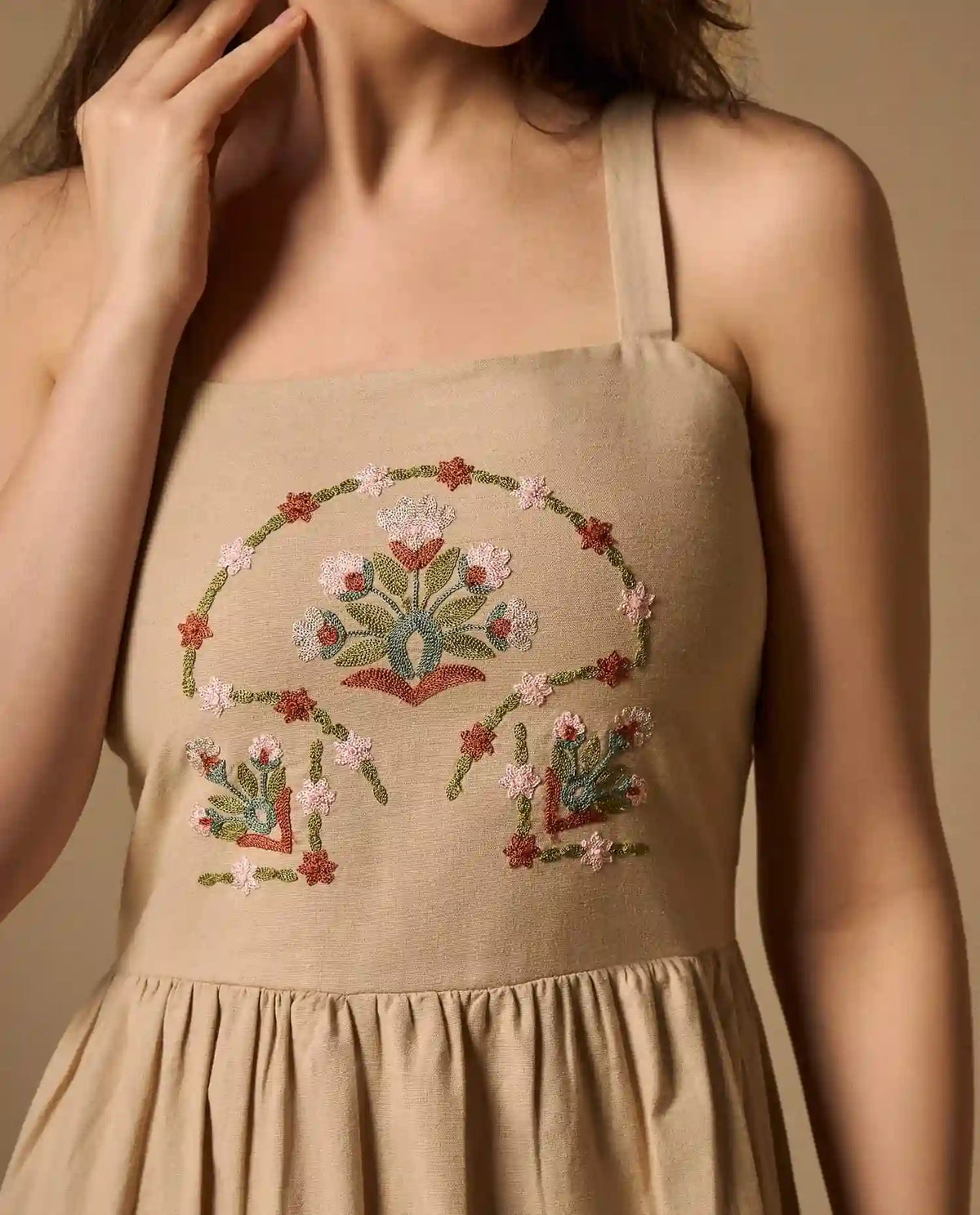 Woman wearing AYRA long beige dress featuring multicolored handcrafted floral embroidery on the structured bodice and hemline