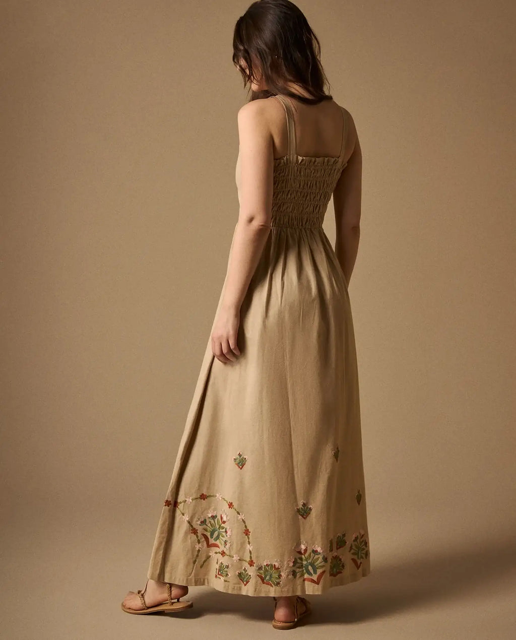 Woman wearing AYRA long beige dress featuring multicolored handcrafted floral embroidery on the structured bodice and hemline