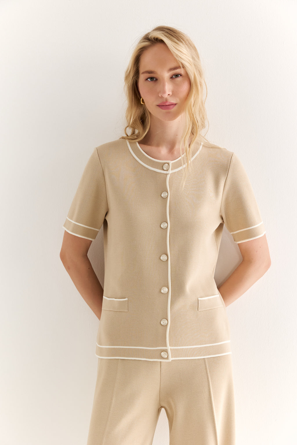 Woman wearing a beige pajama set with white buttons against a plain background