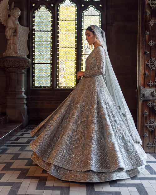 Woman in a silver embroidered traditional outfit standing in a cathedral with stained glass windows.