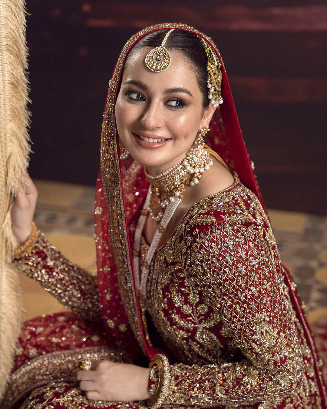 Woman in traditional red and gold bridal outfit with jewelry, smiling.