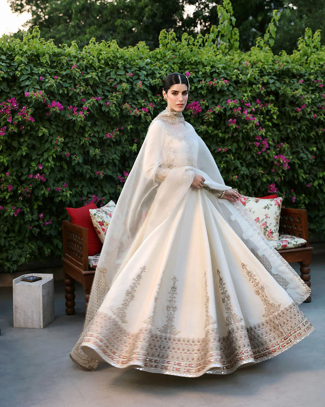 Woman in a white embroidered dress standing in front of a floral bush
