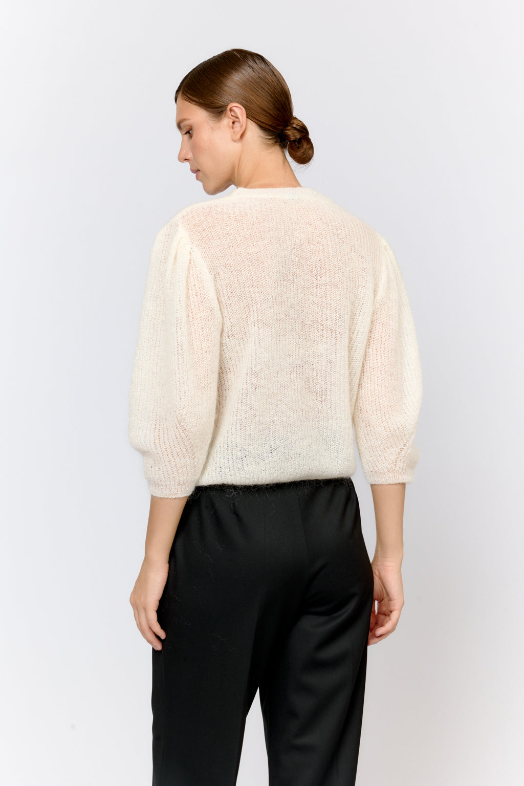 Woman wearing a cream sweater and black pants on a white background