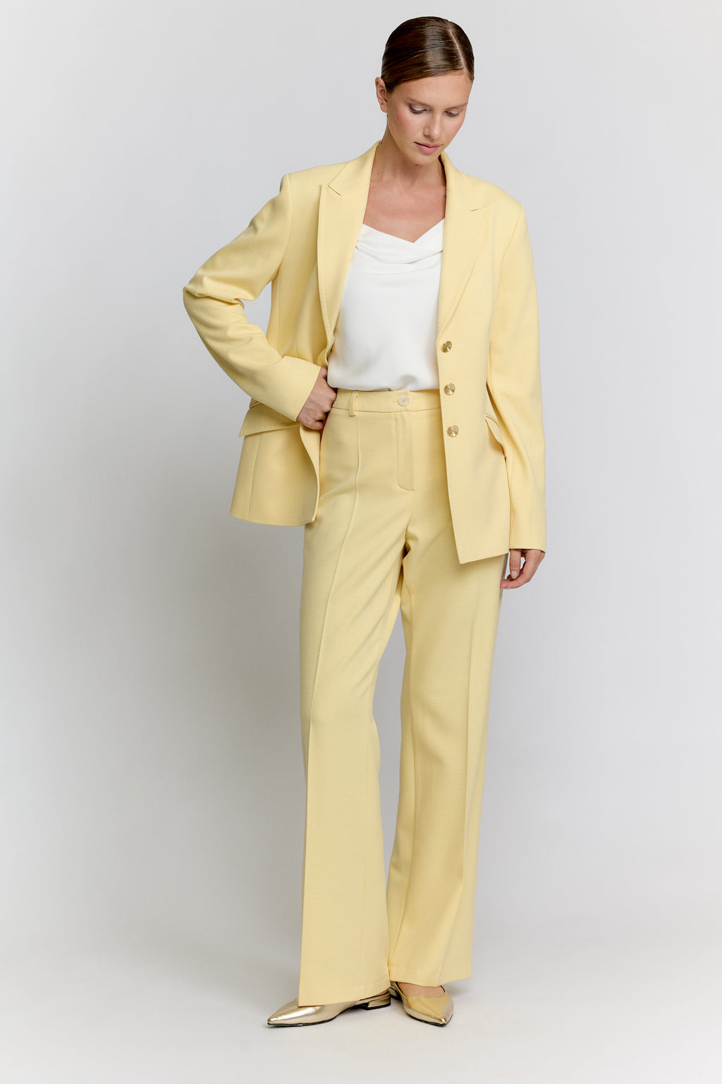 Woman wearing a light yellow suit with a white top on a plain background