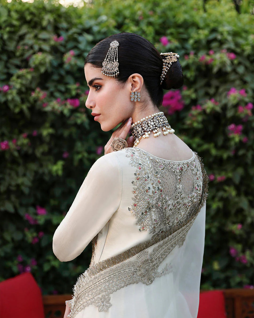 Woman in an embroidered saree with jewelry against a floral background