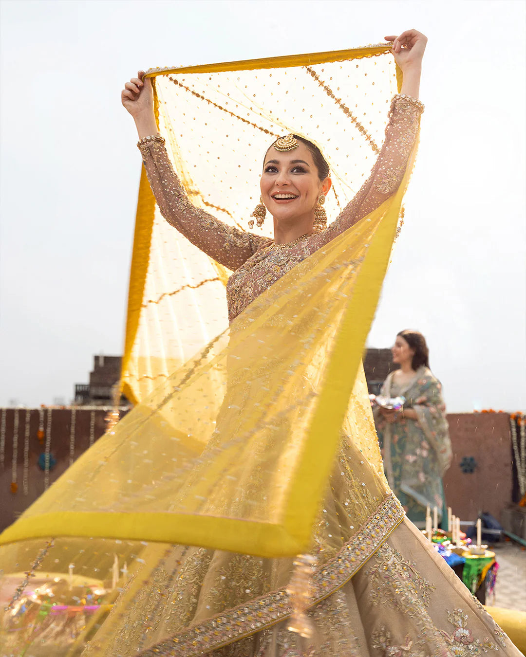 Woman in traditional attire holding a yellow fabric with a scenic background