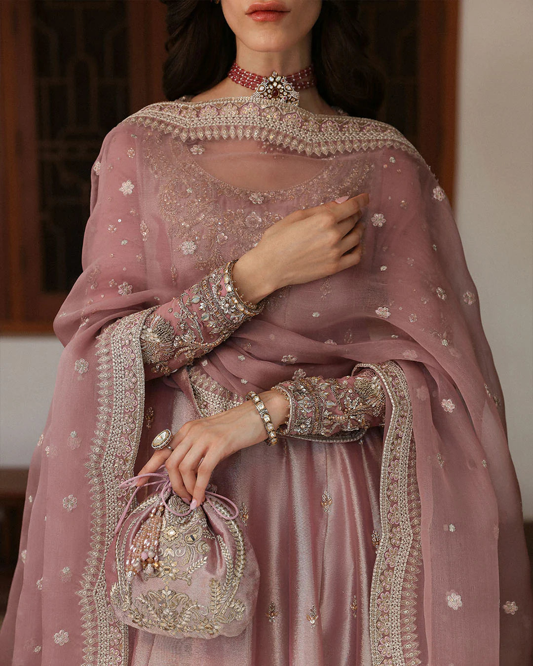 Person wearing a pink embroidered traditional outfit with jewelry and a handbag.