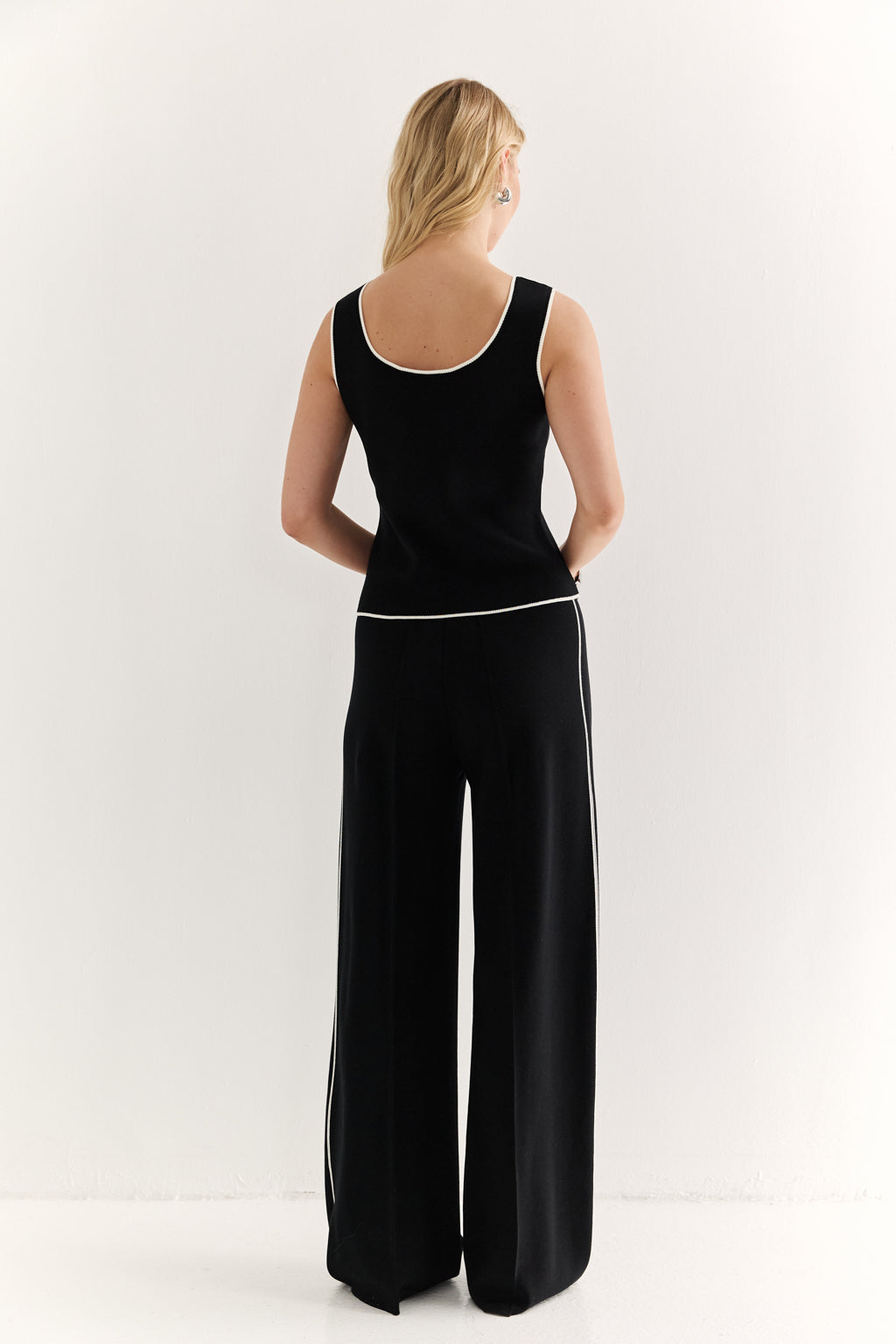 Woman wearing a black sleeveless top and wide-leg pants on a white background